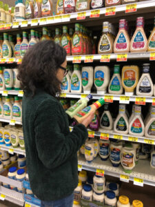 A woman compares two types of dressings in the salad dressing aisle.