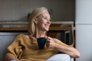 A woman smiles while sitting in a recliner holding a mug of coffee.